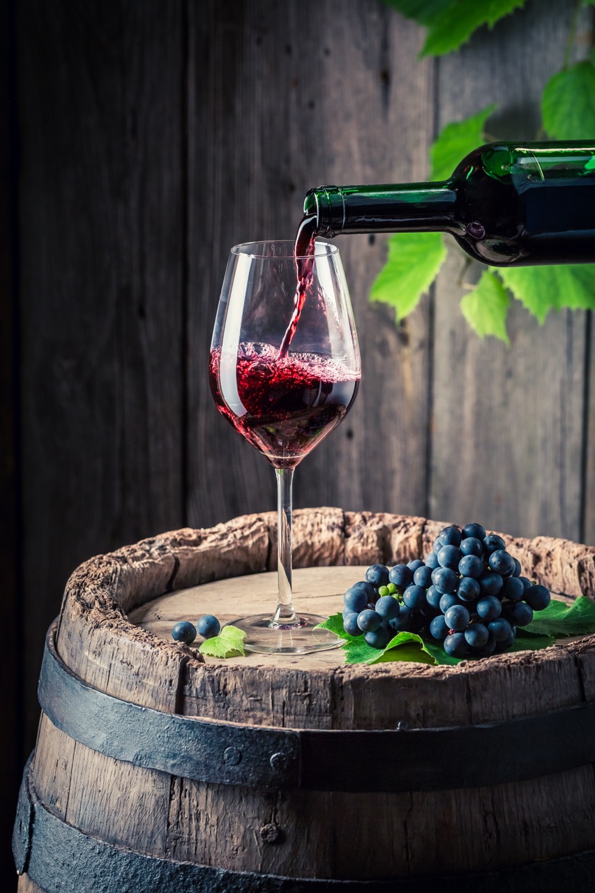 Pouring red wine from bottle into a glass on barrel