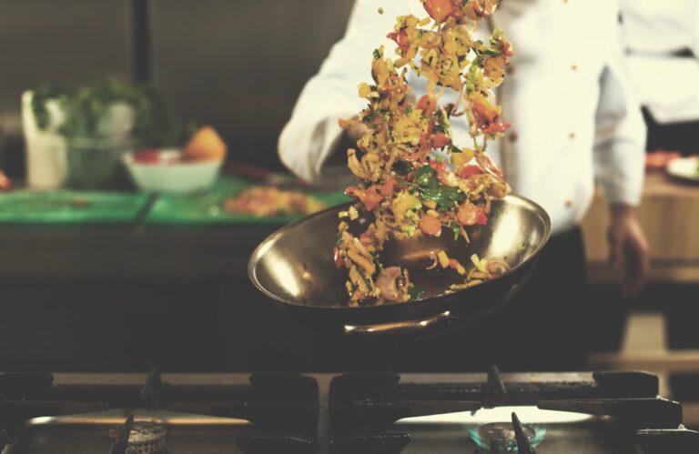 Young male chef flipping vegetables in wok at commercial kitchen