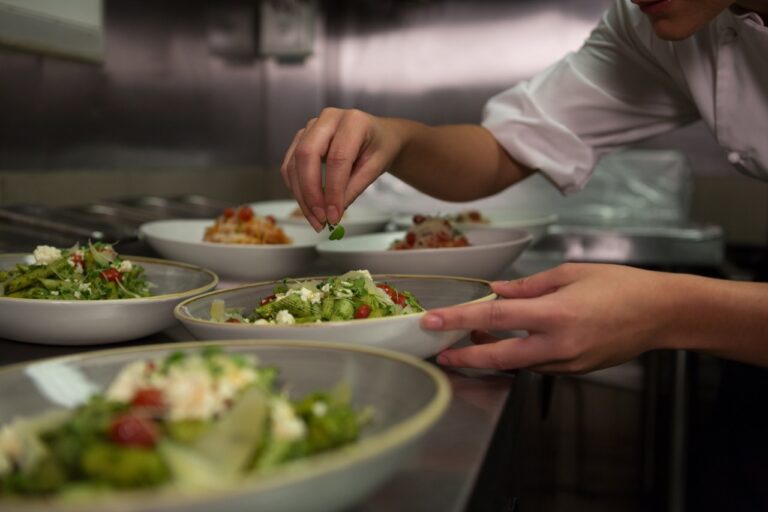Female chef garnishing appetizer plates at order station in commercial kitchen
