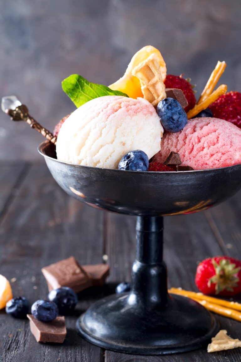 Trio of tasty lemon, vanilla and strawberry flavored frozen dessert ice cream in a metal bowl with wafer straws and berries on wooden
