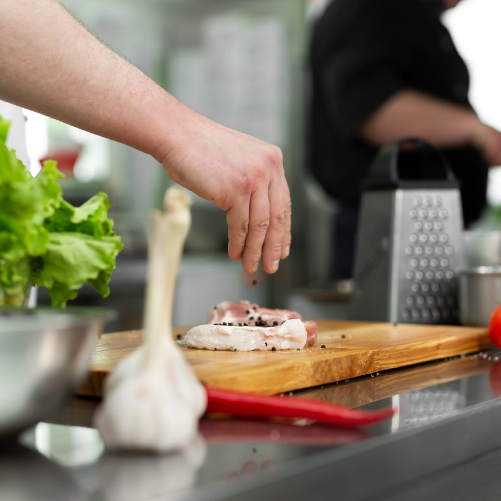 Chef peppering raw beef steak. Professional cook seasoning juicy meat with pepper, salt and herbs before grill