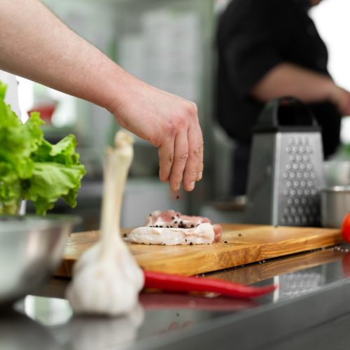 Chef peppering raw beef steak. Professional cook seasoning juicy meat with pepper, salt and herbs before grill