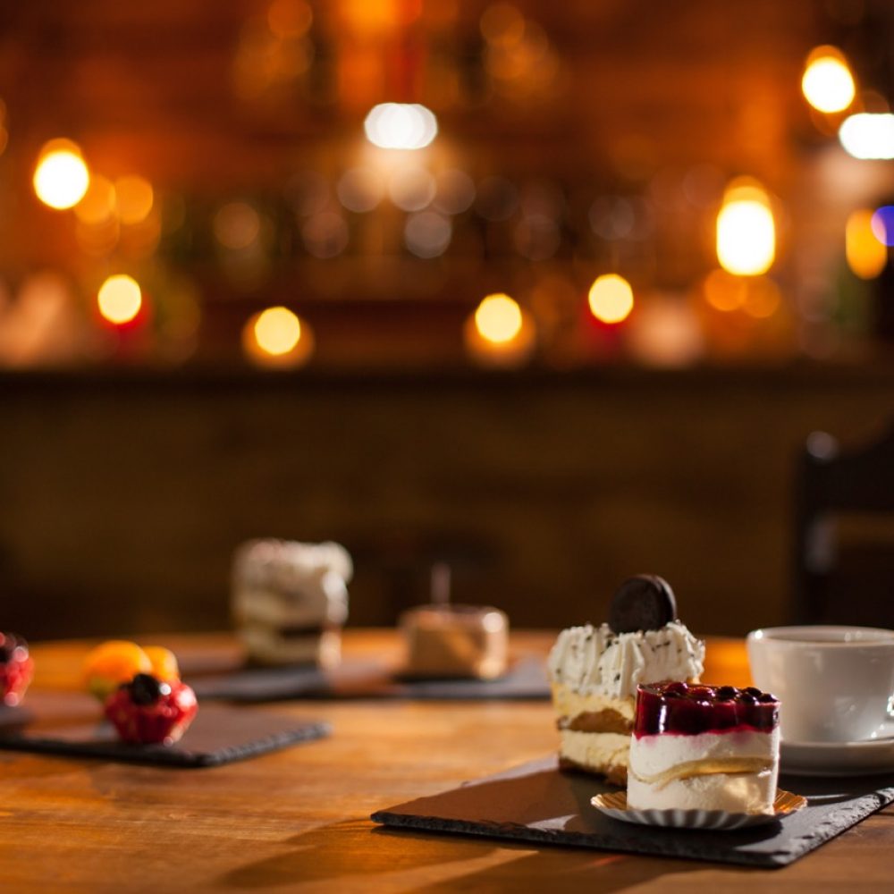 Gorgeous view of different cakes with different flavours over a wooden board in a coffee shop. Delicious variety of cakes in a coffee shop. Tasty cup of coffee.
