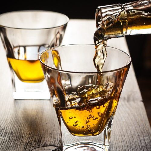 Close-up image of whisky being poured from a bottle into a glass